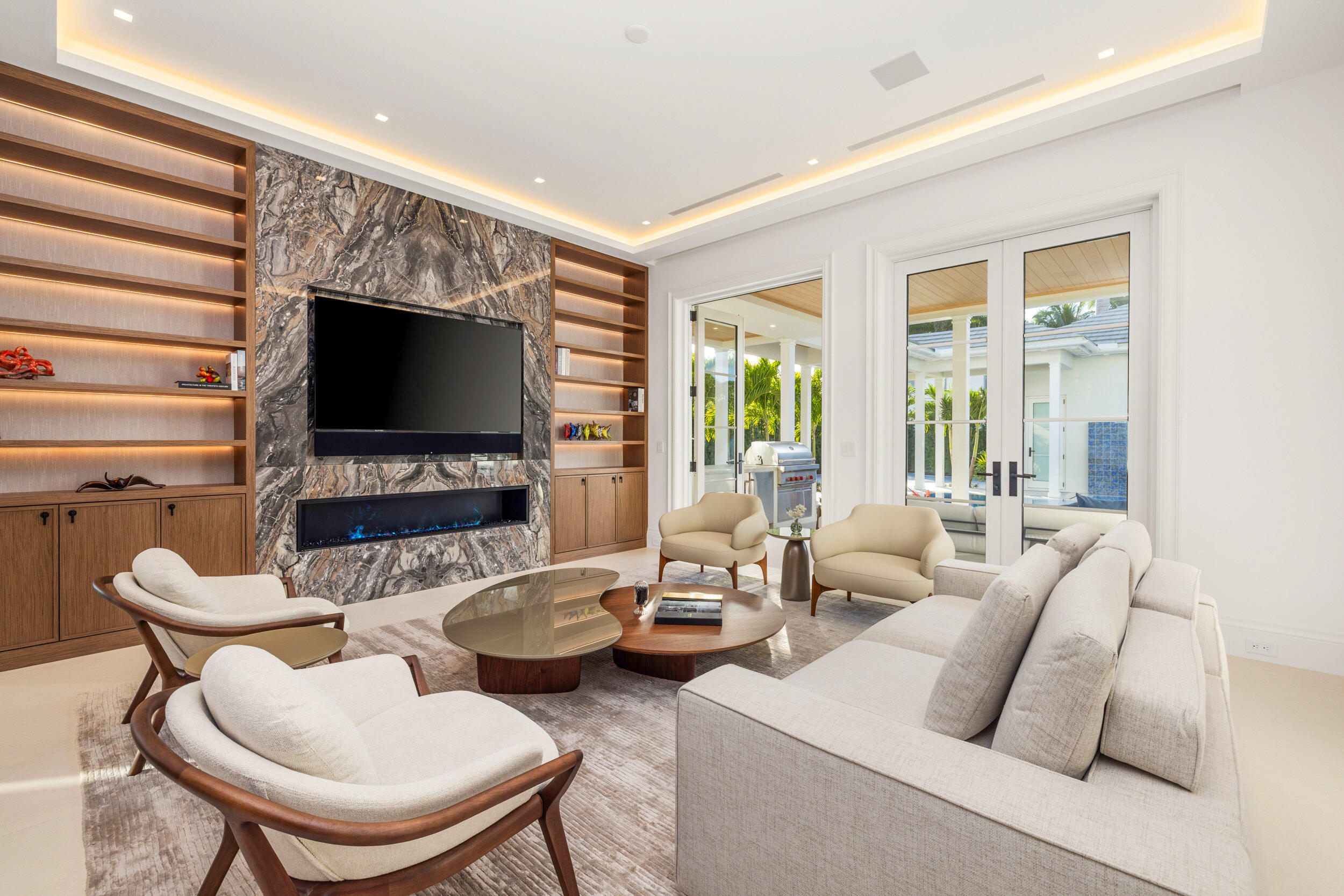 Living room with a marble media wall, linear fireplace, illuminated built-ins, and doors to the patio.