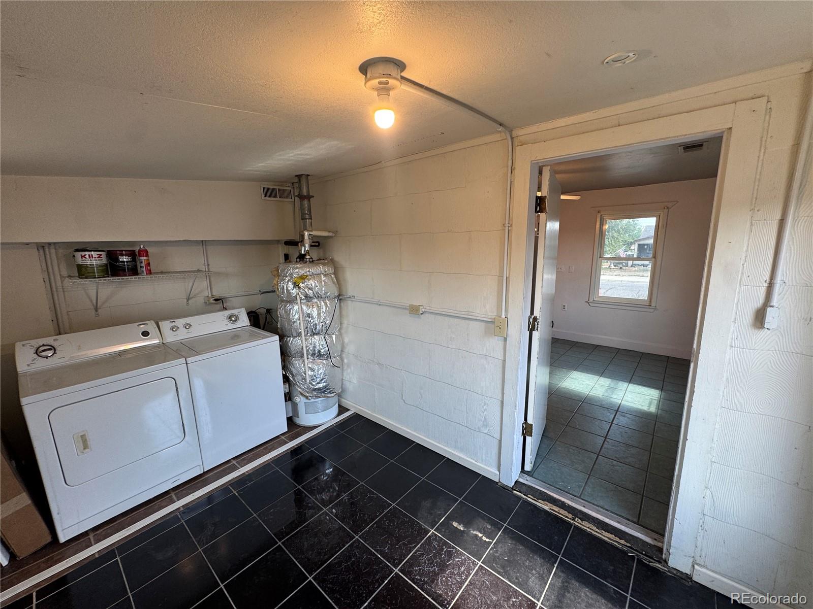 Laundry area with washer, dryer, exposed water heater, and dark tile floor.