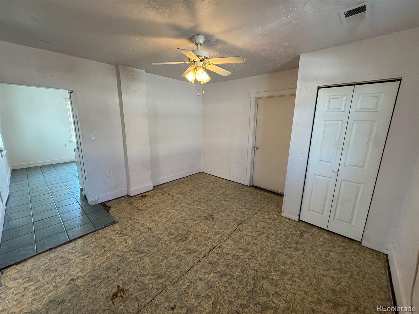 Empty bedroom with a ceiling fan, double-door closet, and worn patterned carpet.