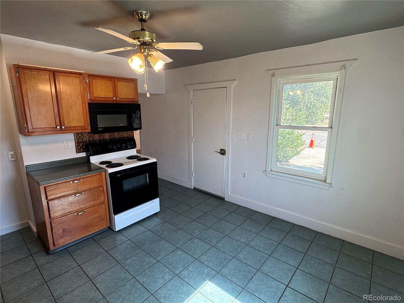 Kitchen with wood cabinets, electric range and microwave, gray tile floor, and a ceiling fan.