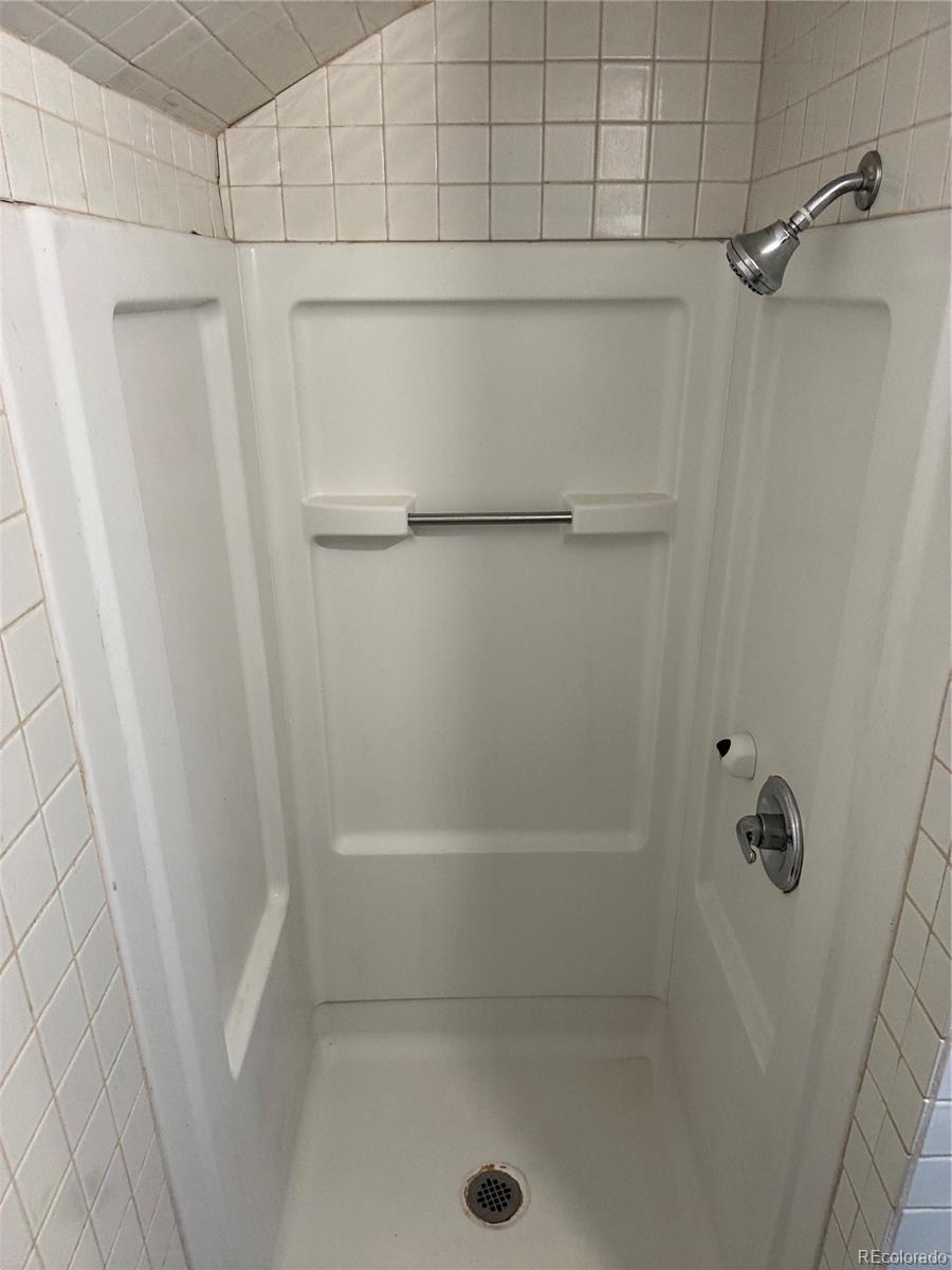 White shower stall with molded shelves, a grab bar, tiled walls, and chrome fixtures.