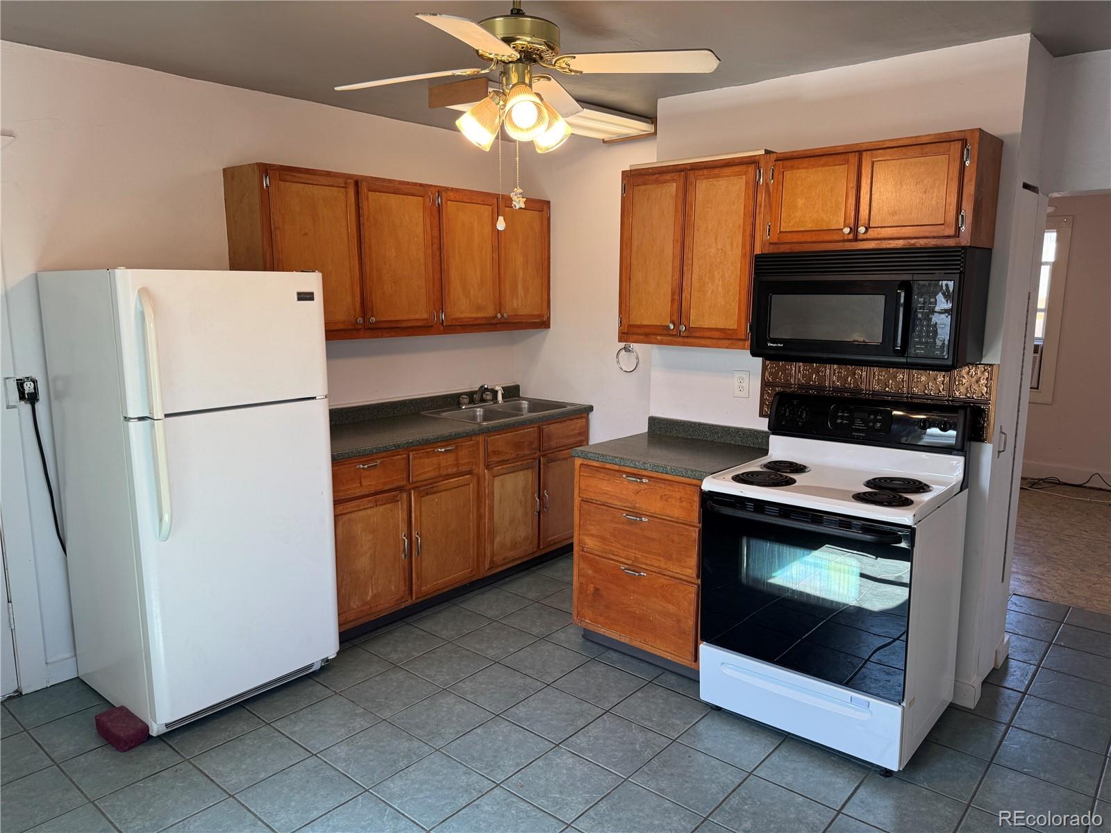 Kitchen with warm wood cabinets, gray tile flooring, and white refrigerator and electric range.