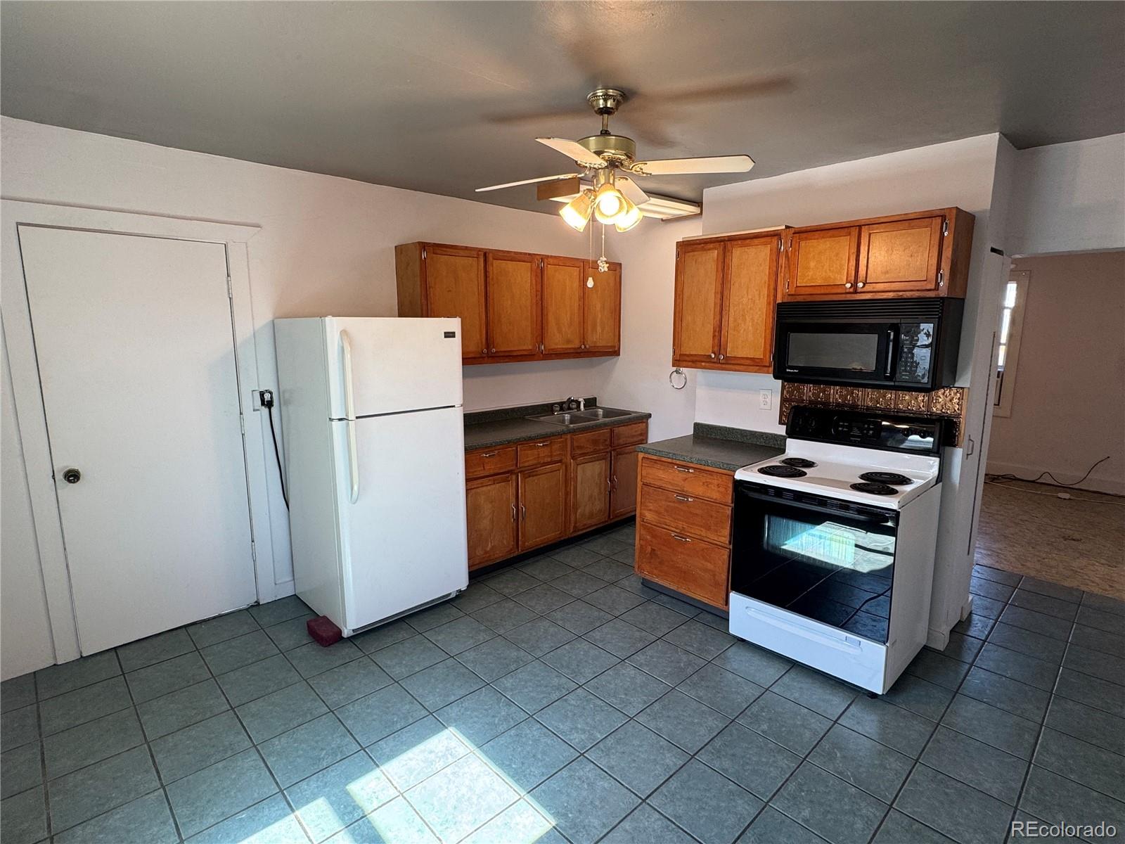Kitchen with wood cabinets, gray tile floors, white refrigerator, and electric range with microwave.