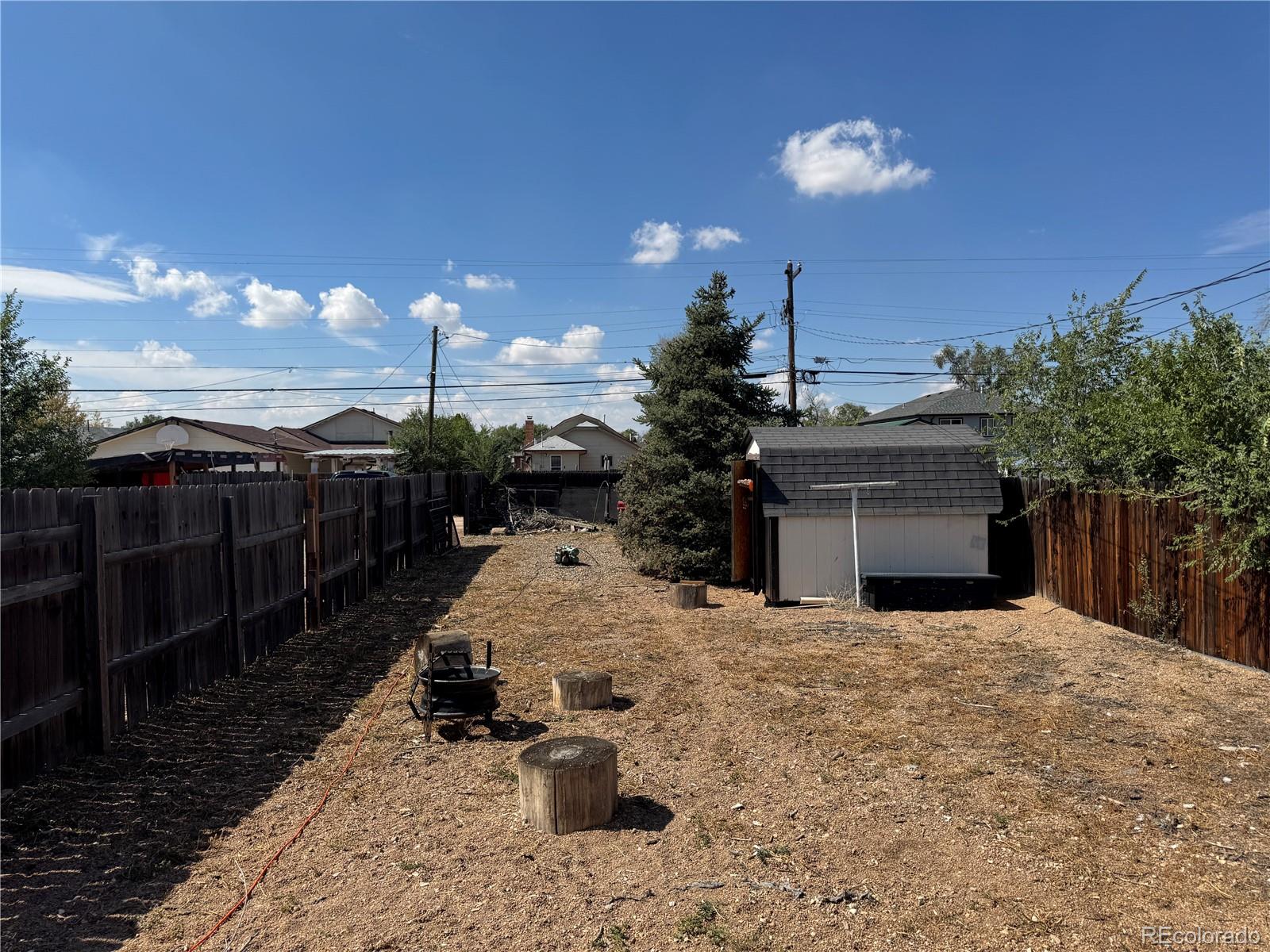 Fenced backyard with a small shed, bare ground, and tree stumps.
