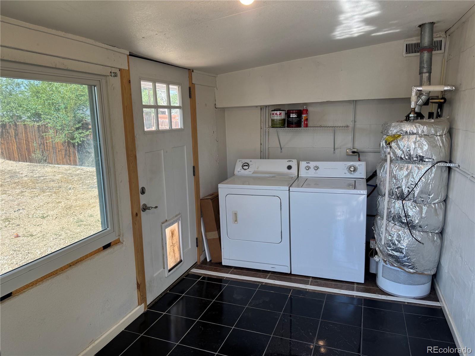 Laundry room with washer, dryer, and foil-wrapped furnace beside a glass exterior door.