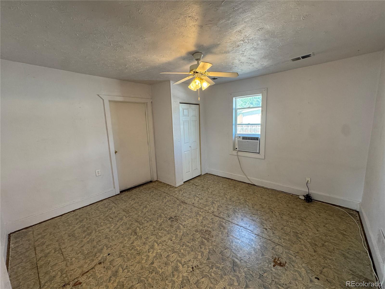 Empty room with patterned flooring, a ceiling fan, two doors, and a window air conditioner.