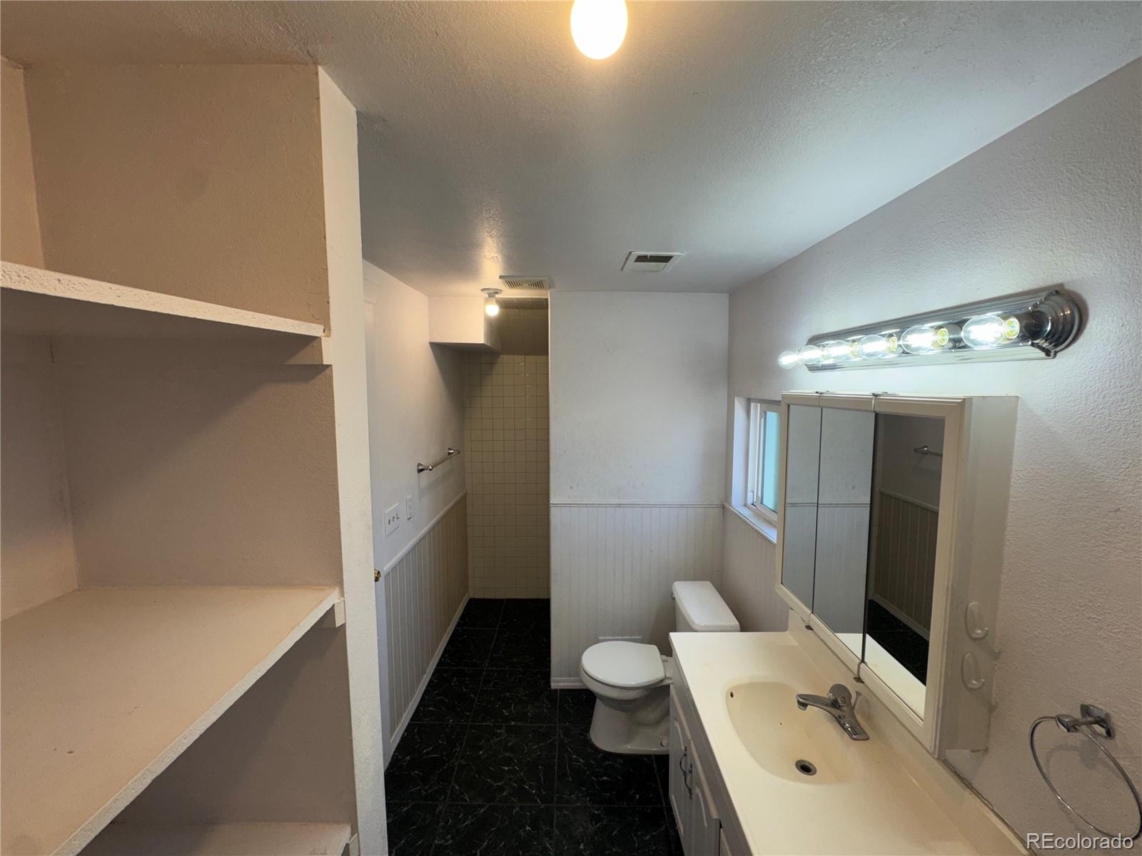 Bathroom with black tile flooring, built-in shelves, a long vanity, and a tiled shower area.
