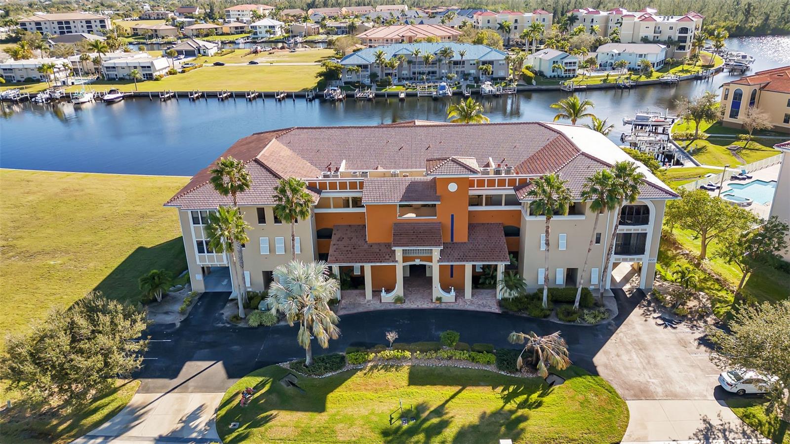 Waterfront condominium with palm trees, canal, docks, and boats behind it.
