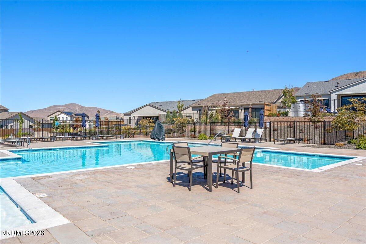 Community pool with a stone-paver deck, outdoor dining set, and mountain backdrop.