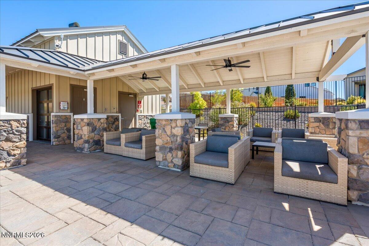 Covered patio with wicker lounge seating, stone columns, and ceiling fans.