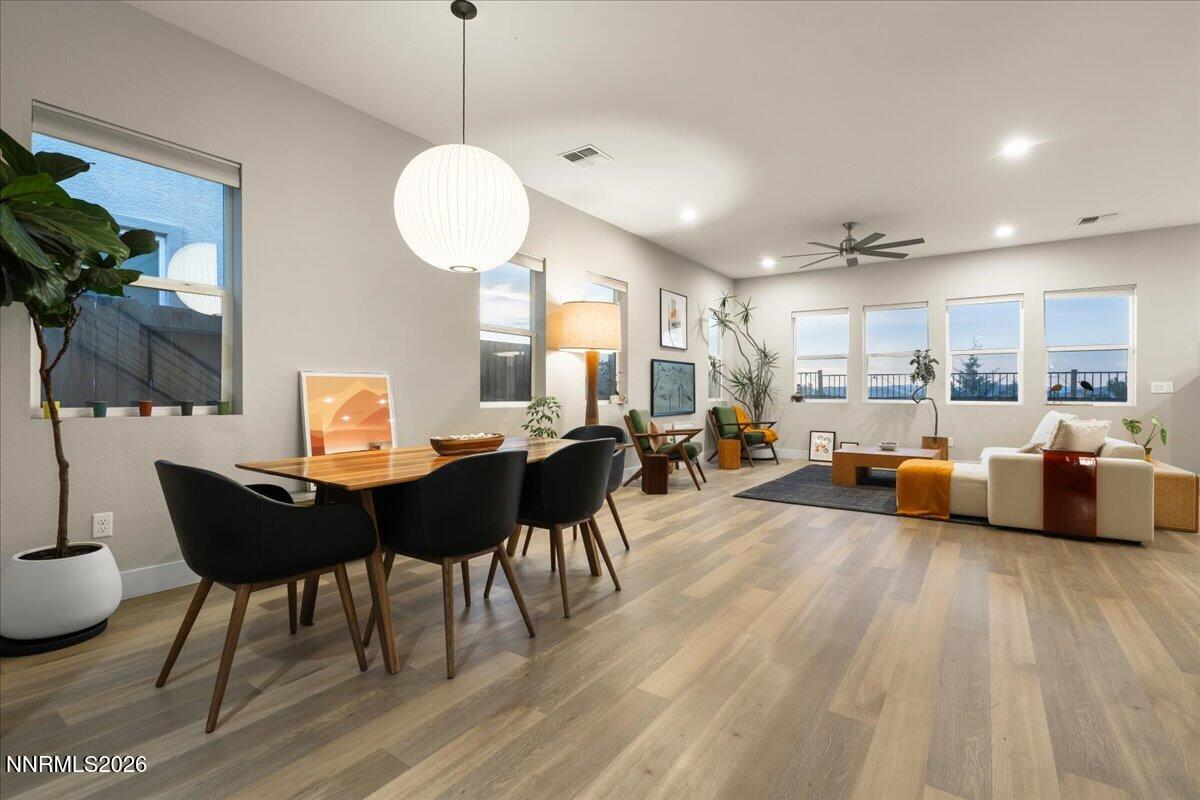 Open-plan dining and living room with a wood table, black chairs, and windows overlooking the outdoors.