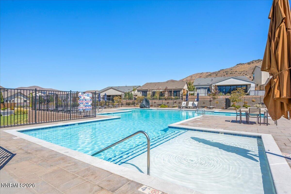 Community swimming pool with attached spa, patio seating, and surrounding desert hills.