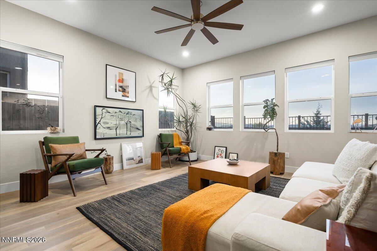 Living room with a white sectional, green chairs, tall windows, and a dark wood ceiling fan.