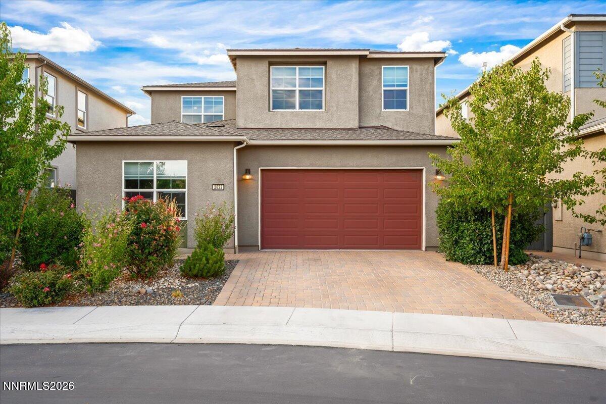 Two-story gray stucco house with a red double garage door and landscaped front yard.