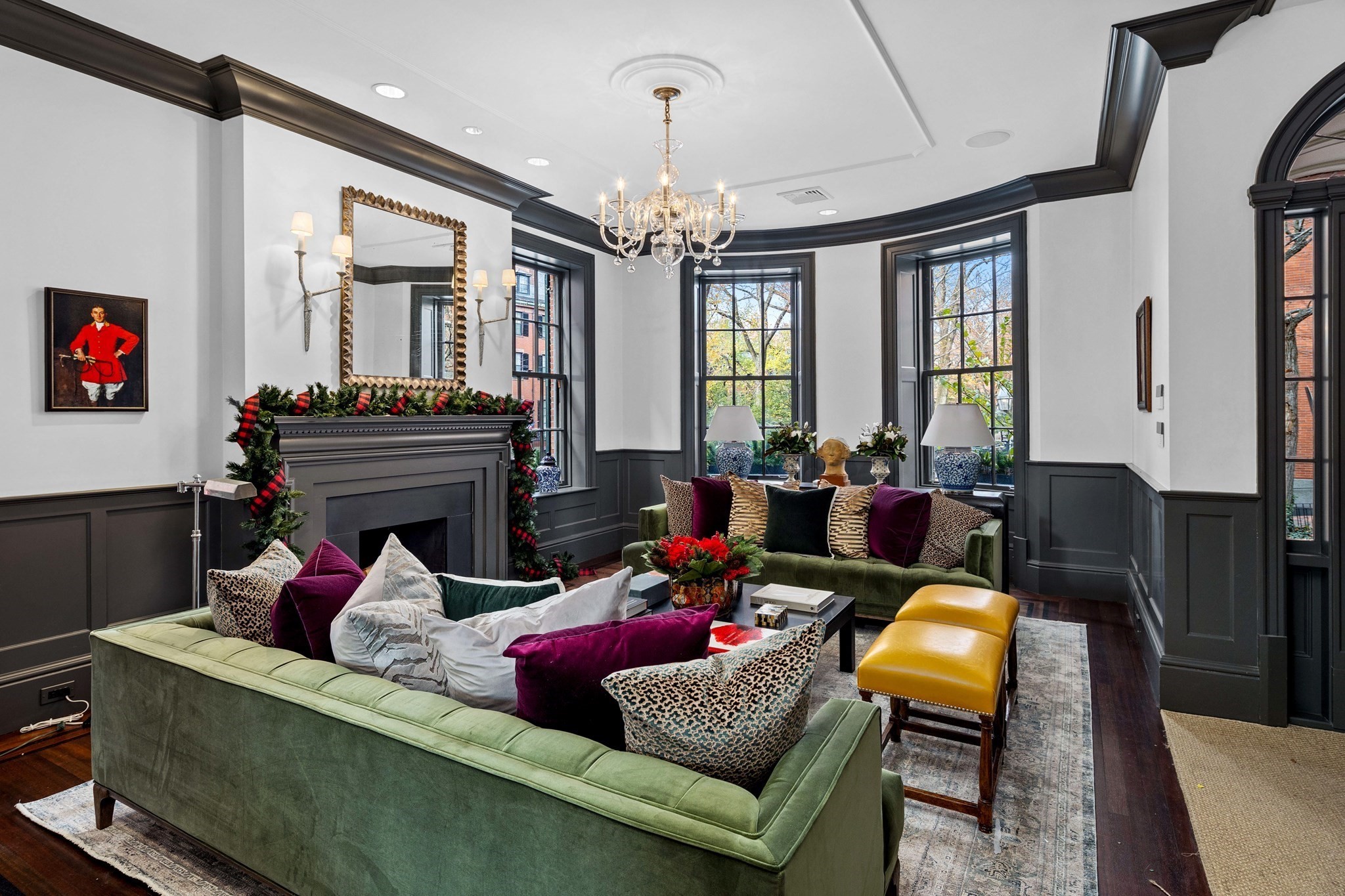 Living room with green sofas, a garland-decorated fireplace, and tall bay windows.