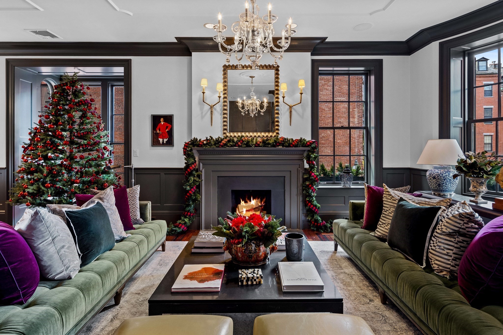 Living room with a lit fireplace, green sofas, chandelier, and decorated Christmas tree.