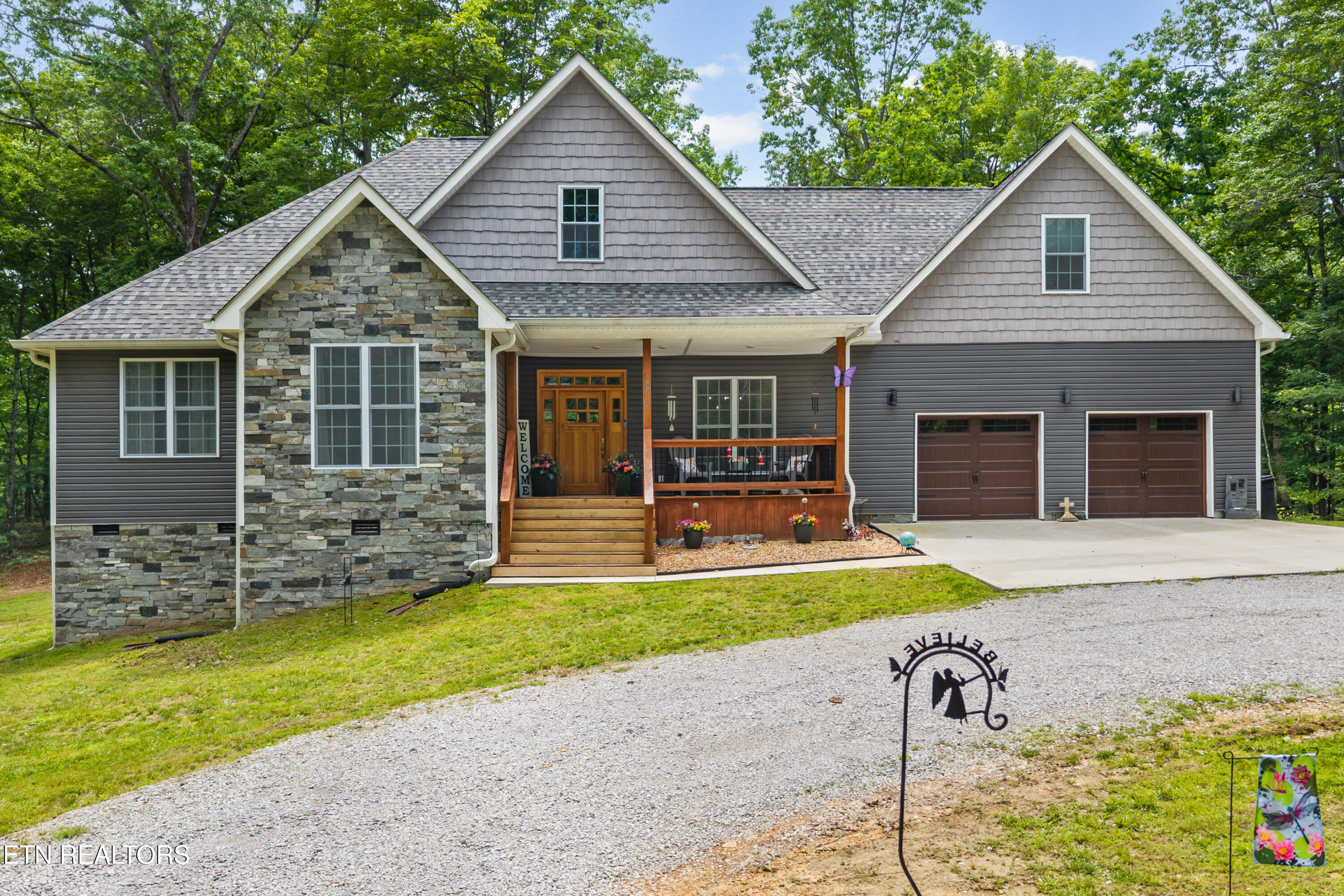 Gray two-story home with a stone facade, covered wood porch, and attached two-car garage.