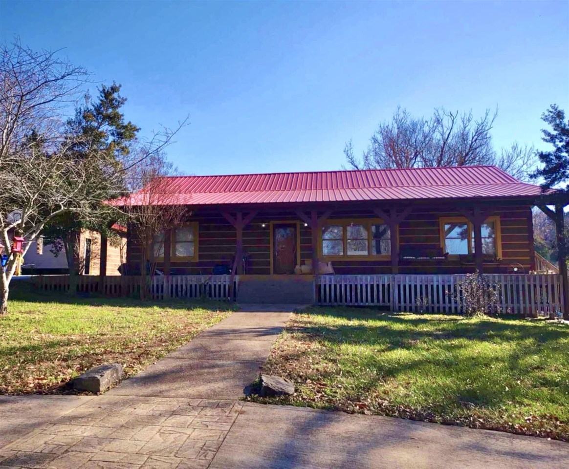 Log cabin-style home with a red metal roof, covered porch, and walkway through the yard.