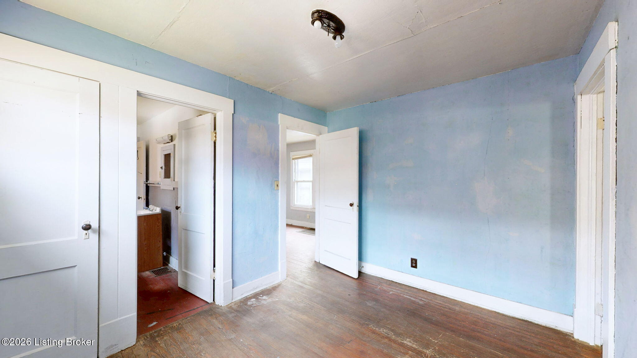 Vacant blue room with worn hardwood floors and open doorways to adjoining rooms.