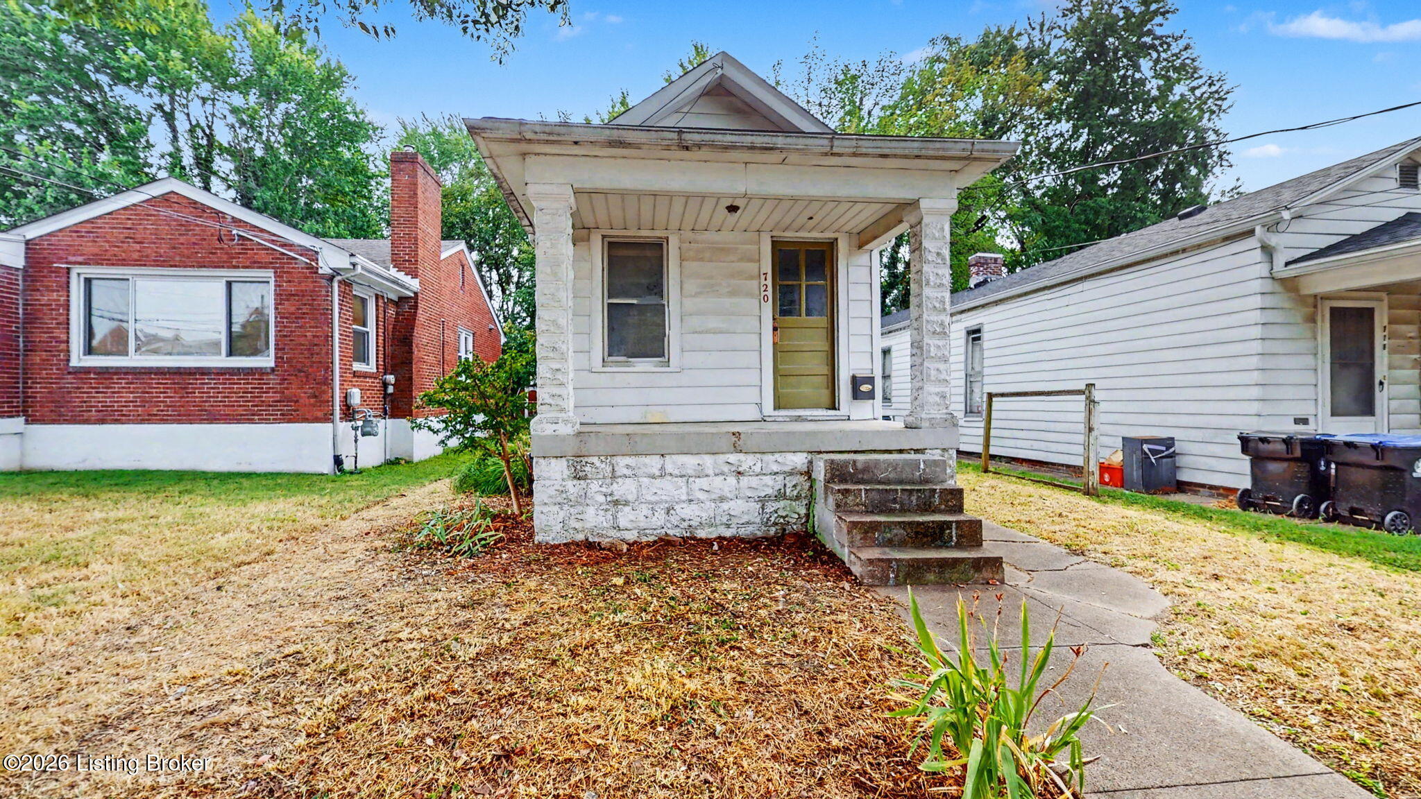 Small white house with a broad covered porch, stone columns, and concrete front steps.