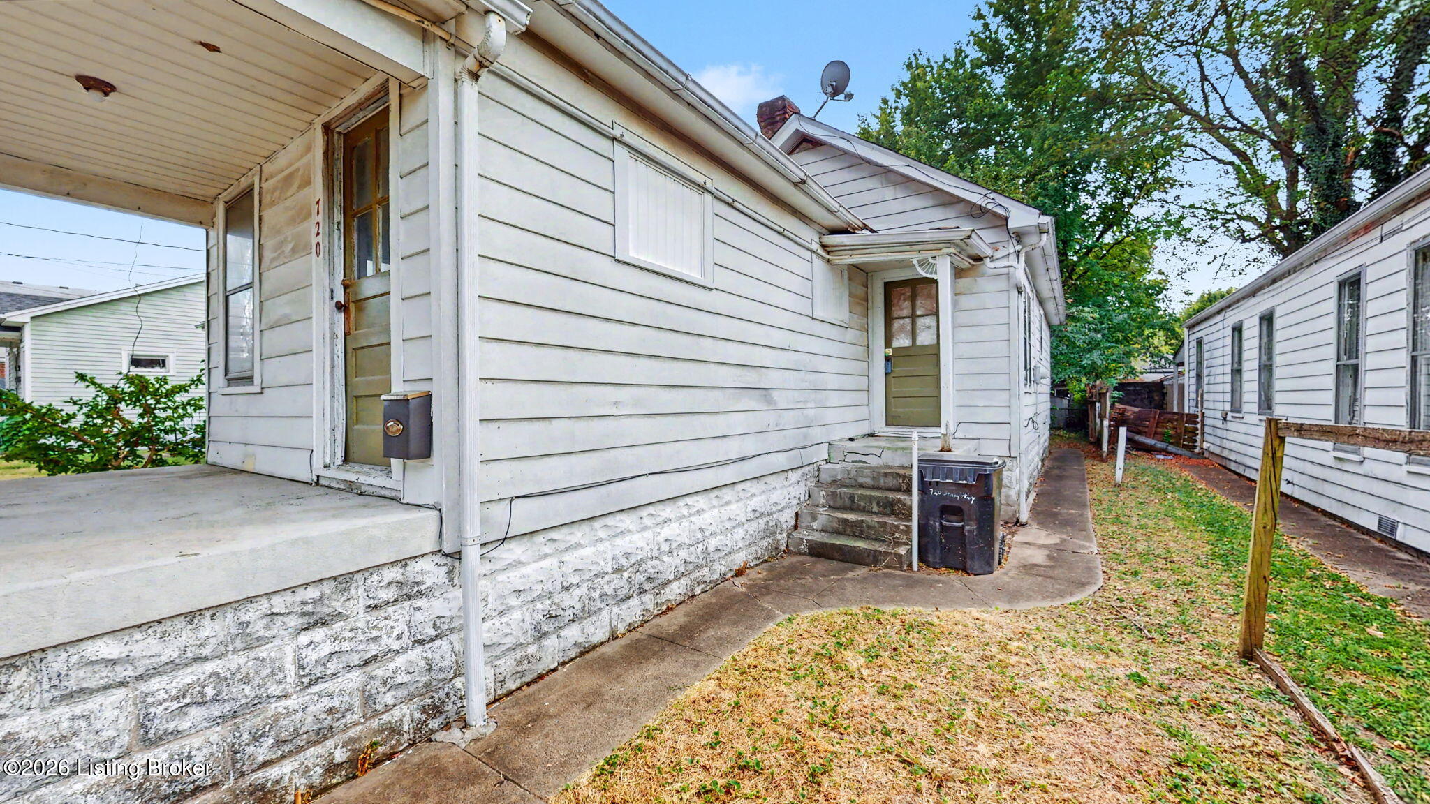 Side exterior of a white-sided home with two entrances, a stone foundation, and a narrow walkway.
