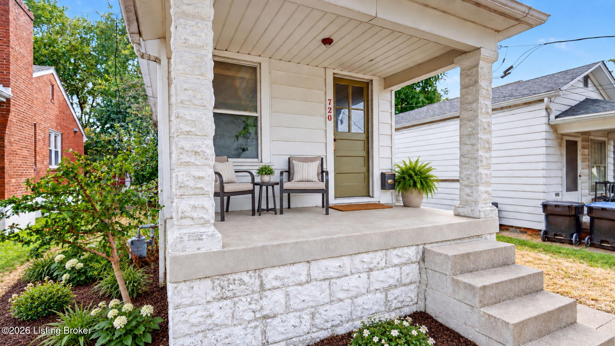 Home’s covered front porch with white stone pillars, two chairs, and landscaped flower beds.