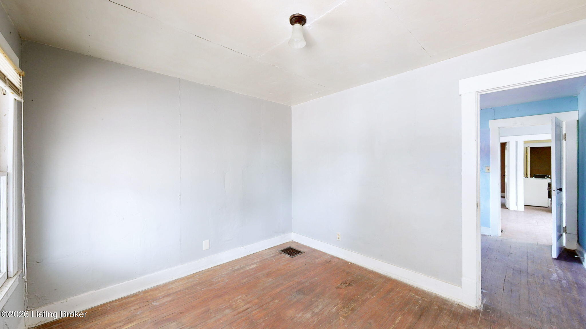 Empty room with worn hardwood floors, a ceiling light, and an open doorway to a blue-painted room.