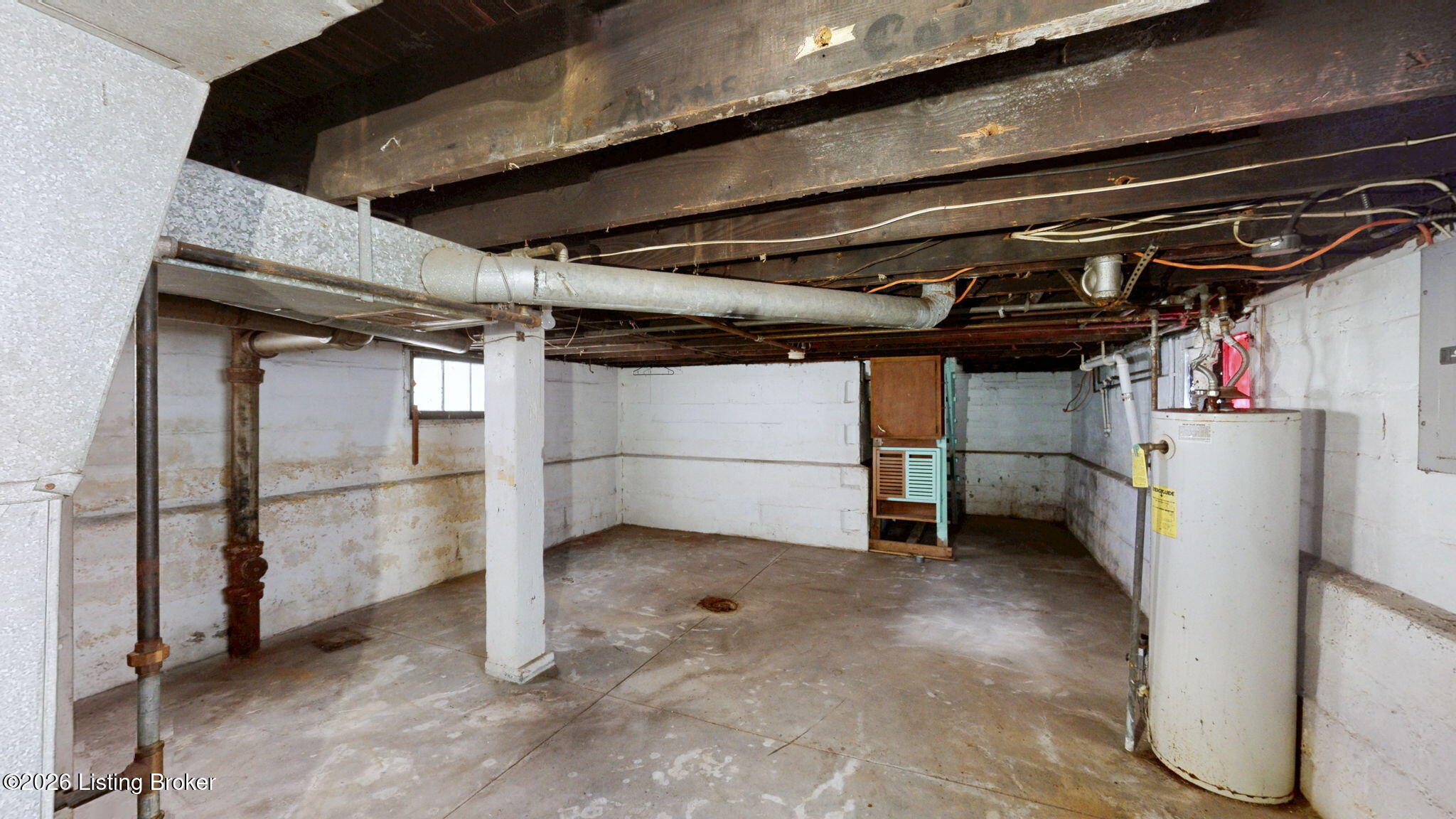 Unfinished basement with exposed joists, overhead plumbing, concrete floor, and water heater.