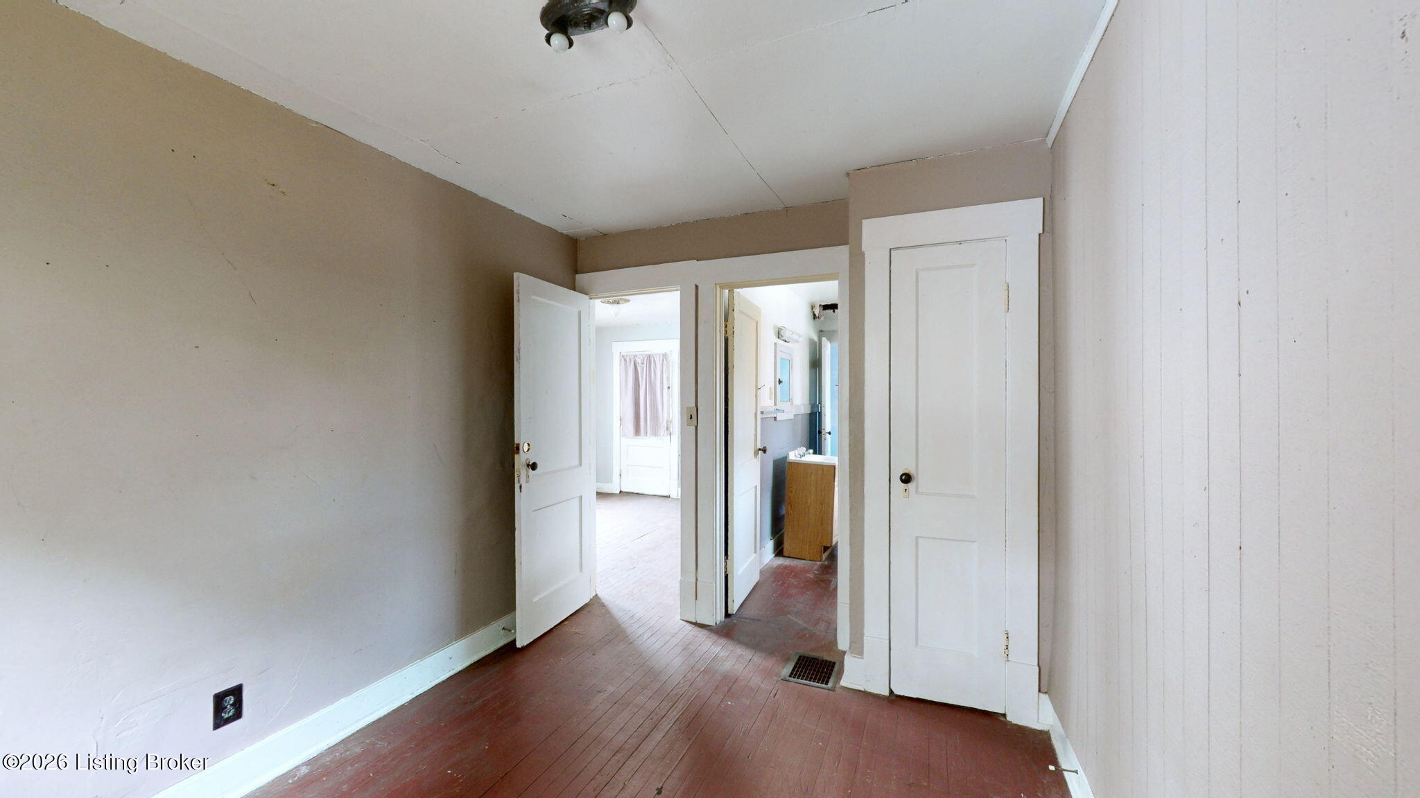 Empty room with worn hardwood floors and open doors to adjoining rooms.