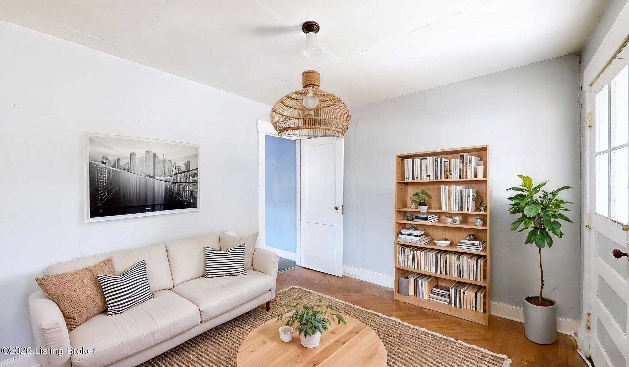 Living room with a cream sectional, woven pendant light, wood bookcase, and herringbone floor.