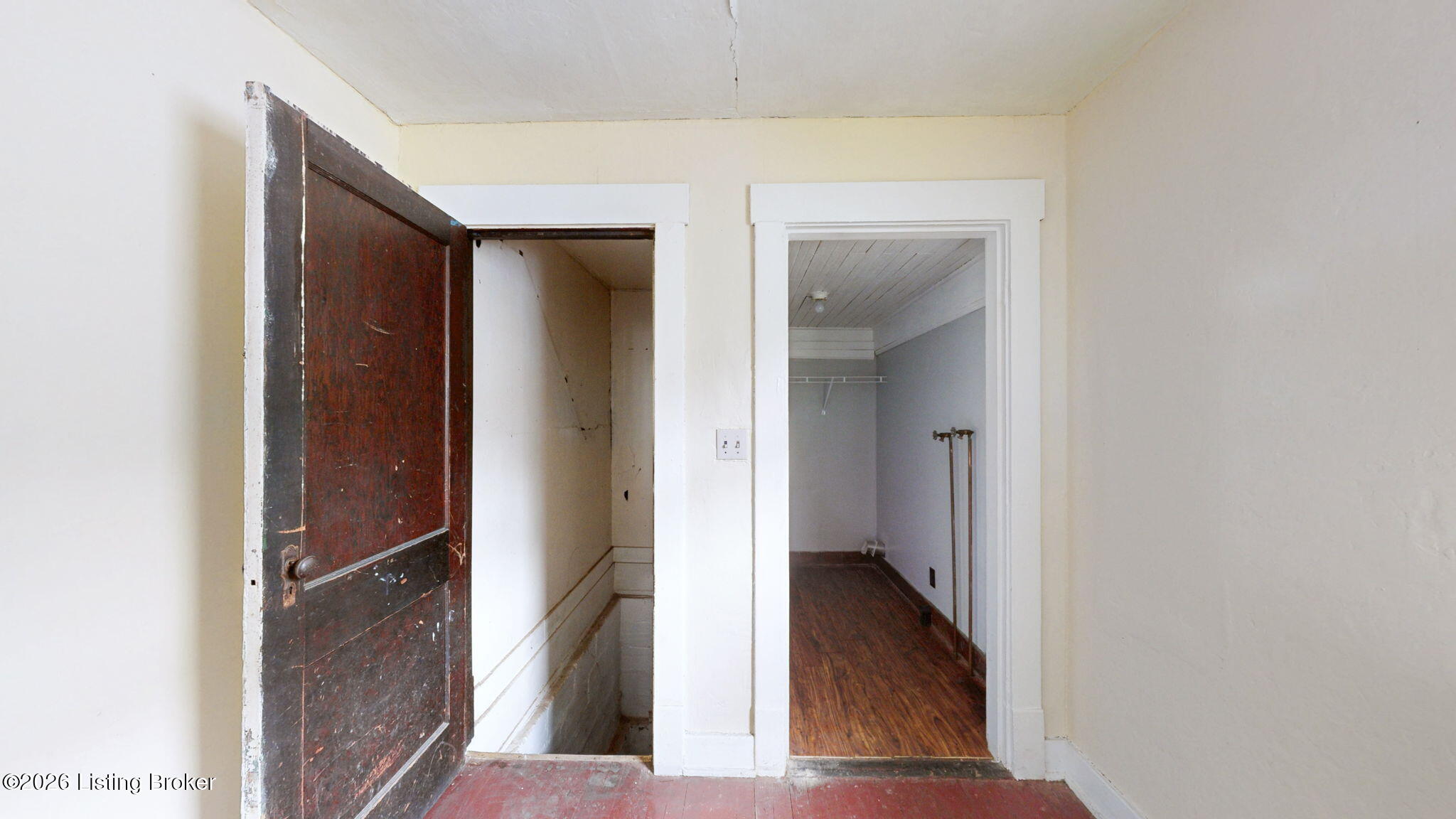 Interior with an open, worn wooden door, stairwell opening, and narrow room with wood flooring.