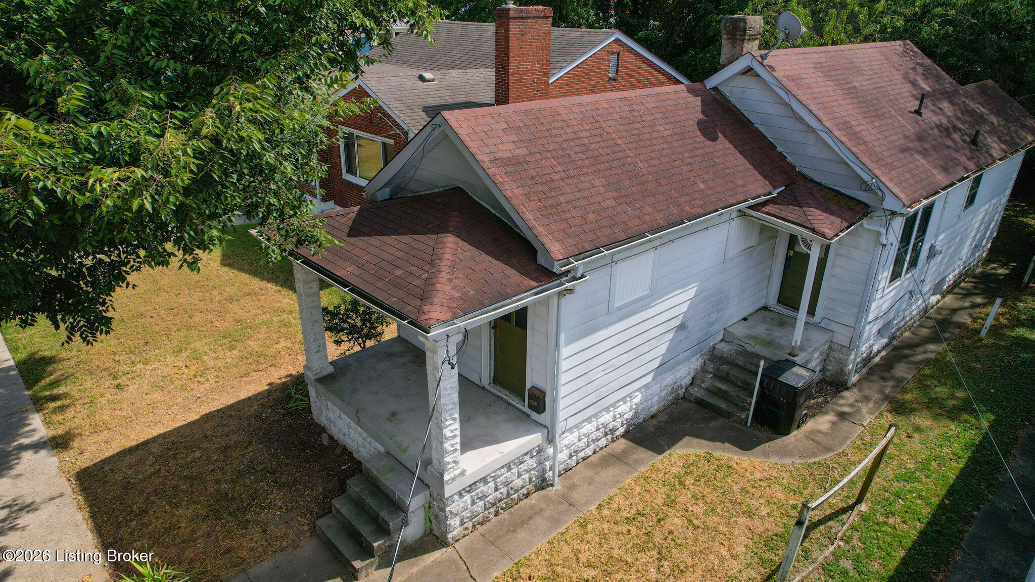 Elevated view of a white-sided house with stone foundation, covered porch, and intersecting shingle roofs.