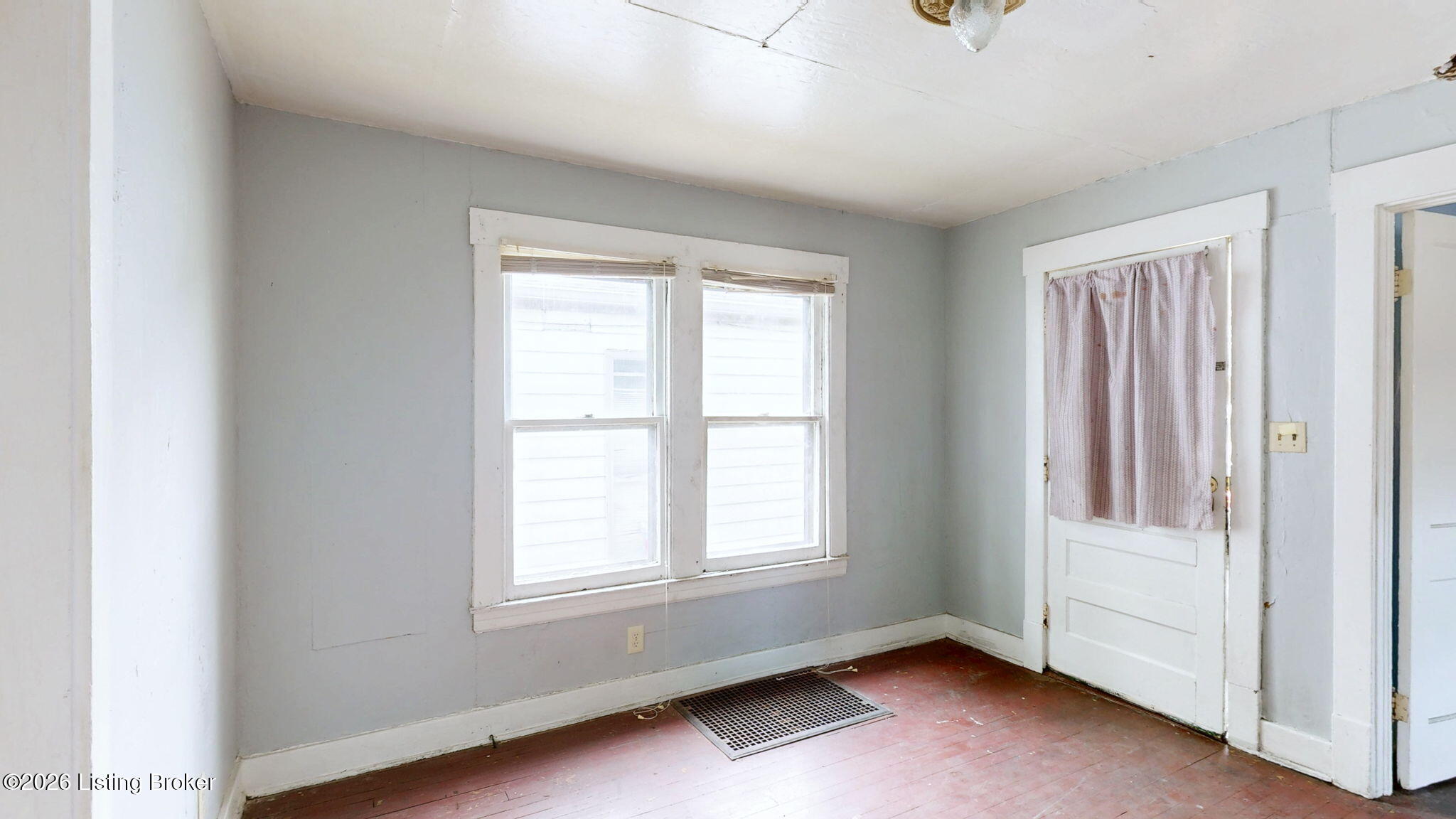 Empty room with paired windows, worn hardwood floors, and a curtained door.