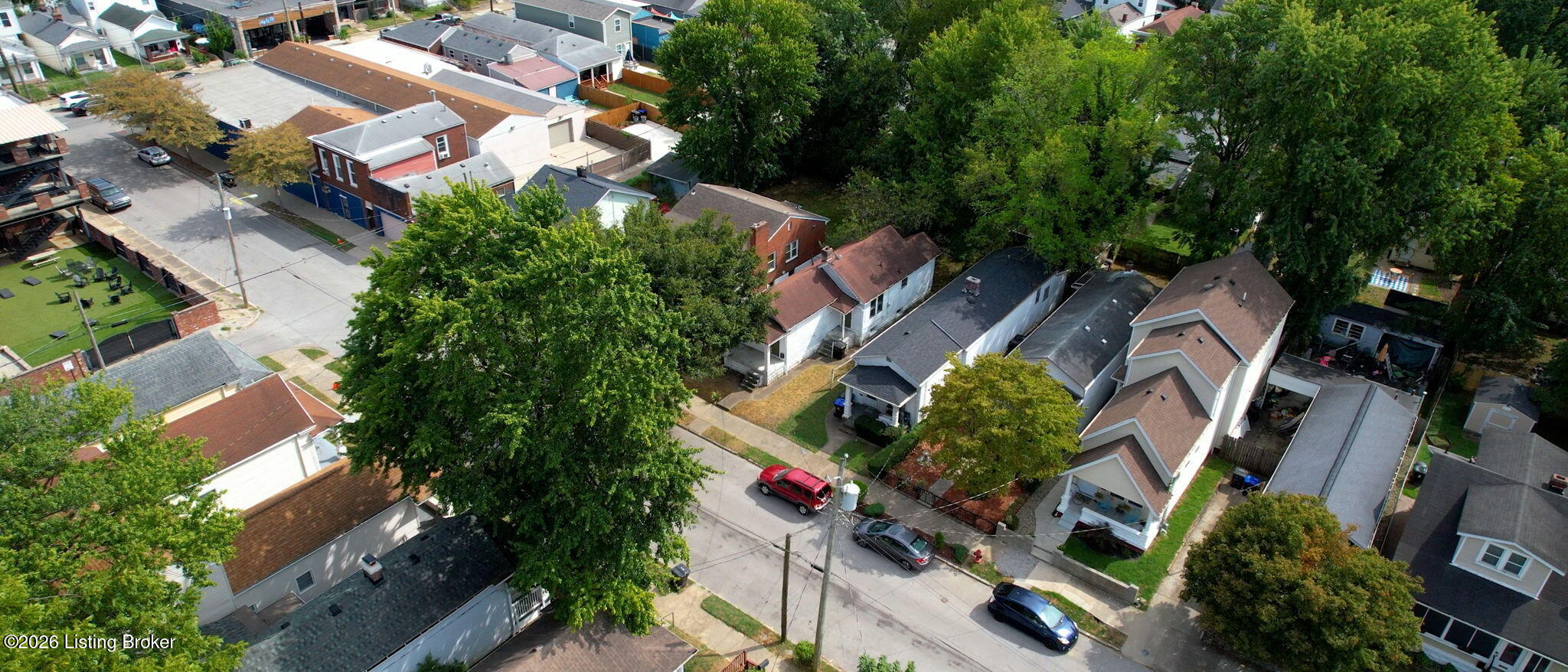Aerial view of a tree-lined residential street with closely spaced homes and parked cars.