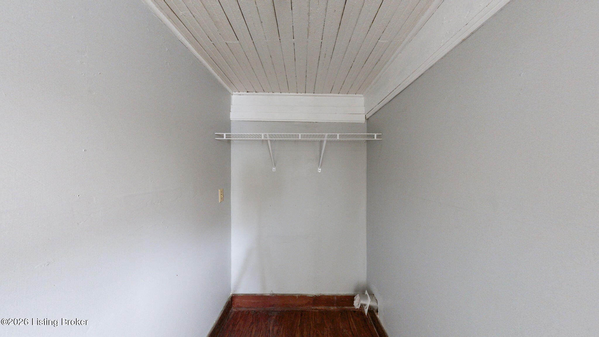Empty closet with a white wire shelf, plank ceiling, and dark wood floor.