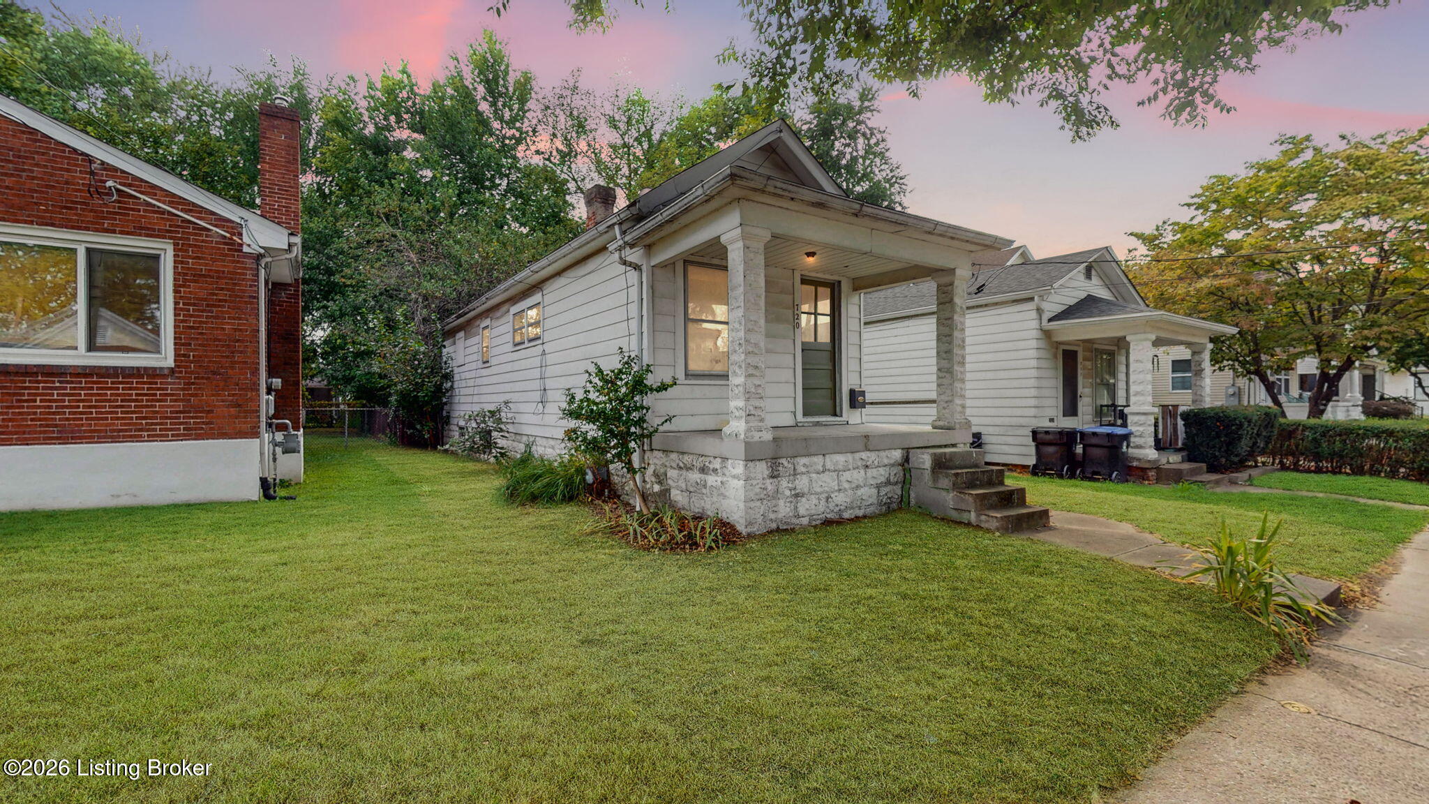 White-sided house with a stone-column porch and front lawn at dusk.