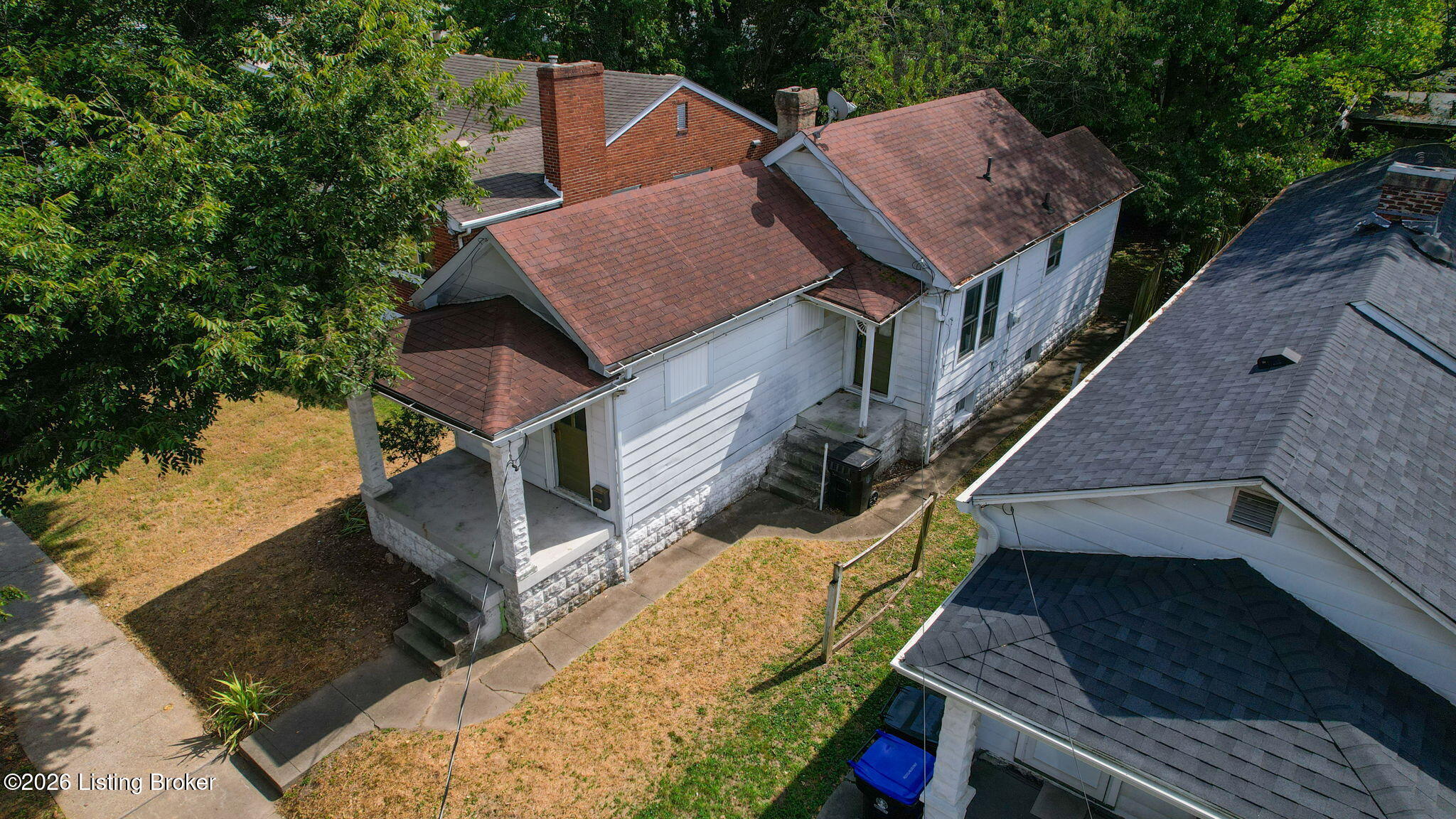 Aerial view of a white-sided house with a red-brown roof, stone foundation, and small covered porch.