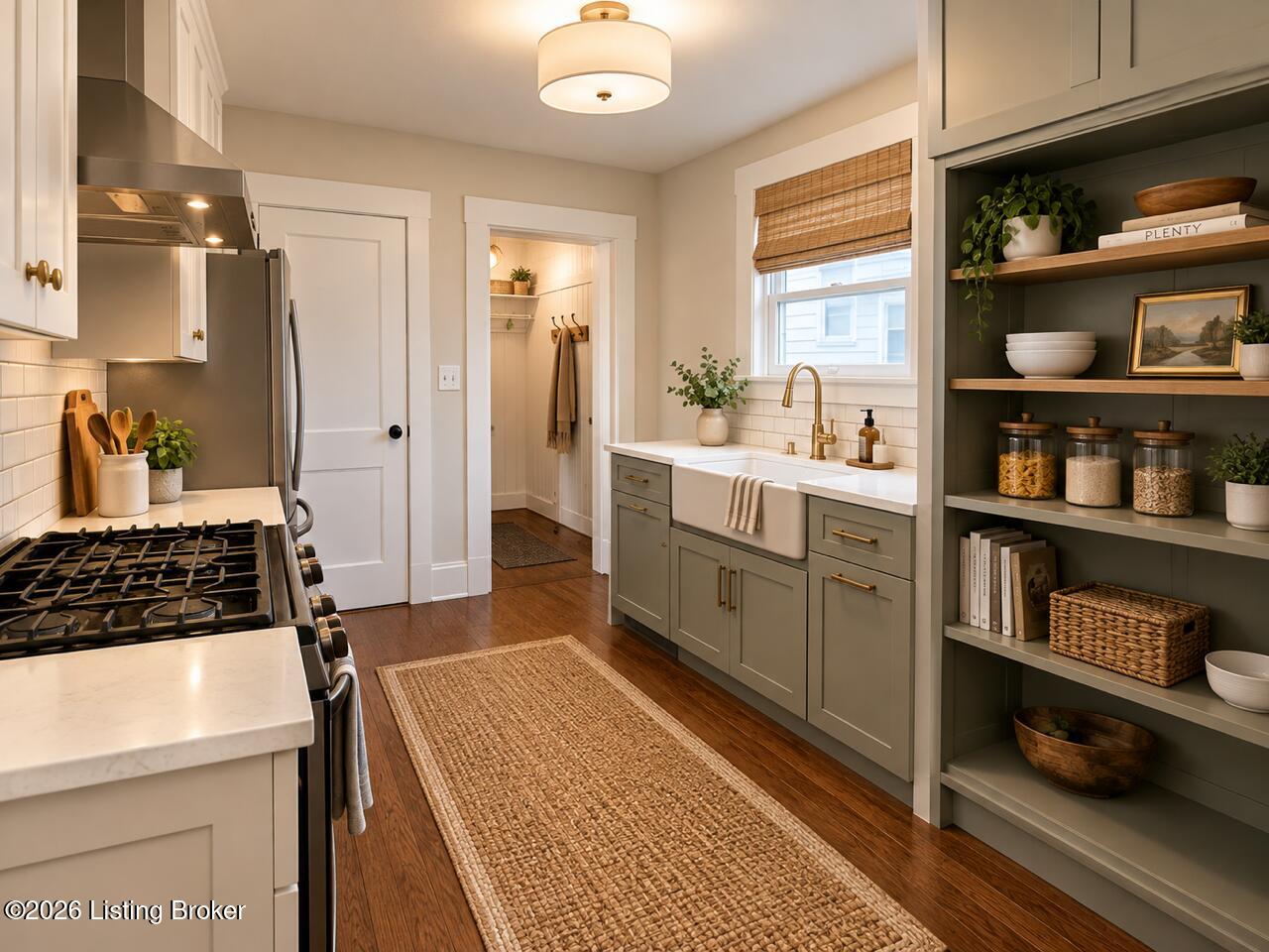 Renovated kitchen with a farmhouse sink, brass fixtures, muted green cabinets, and open pantry shelving.