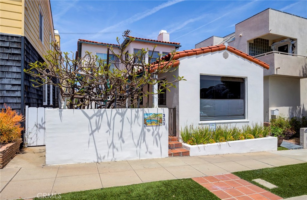 White stucco home with a red tile roof and low courtyard wall along the sidewalk.