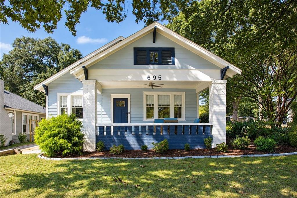 Blue-and-white bungalow with a covered porch, blue railing, and mature trees.
