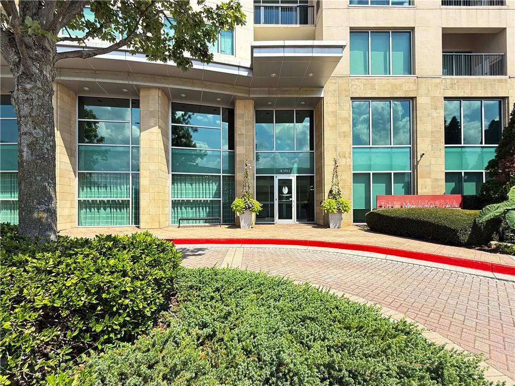 Condominium entrance with a pale stone facade, glass windows, and landscaped grounds.