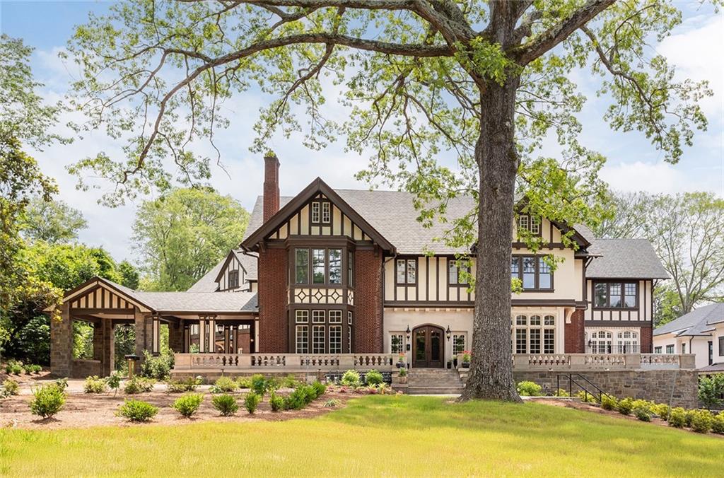 Tudor-style brick home with cream half-timbering, framed by a large tree and broad front lawn.