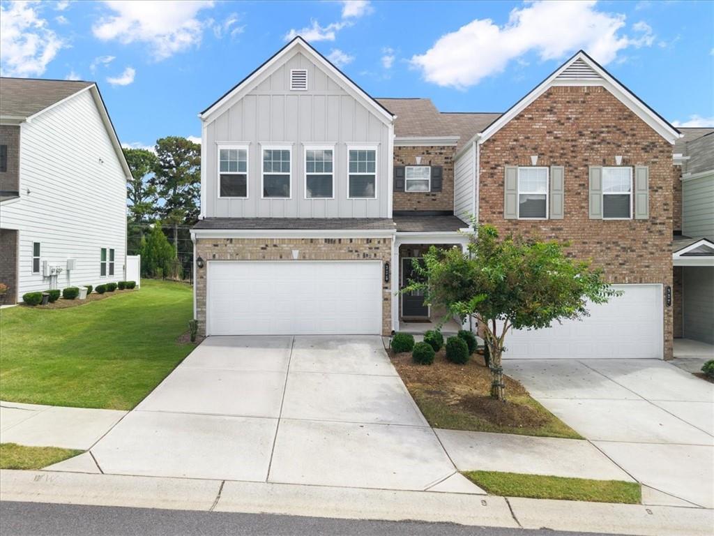 Attached two-story home with brick and white siding, double garage doors, and a small front-yard tree.