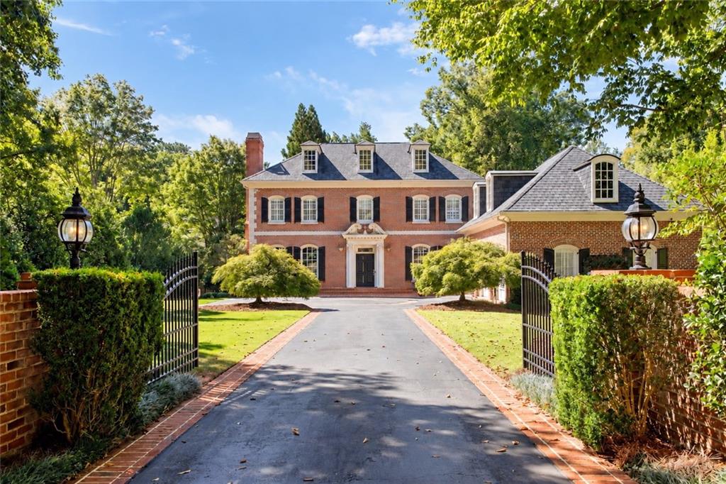 Red brick home with dormer windows, framed by open gates and a brick-edged driveway.