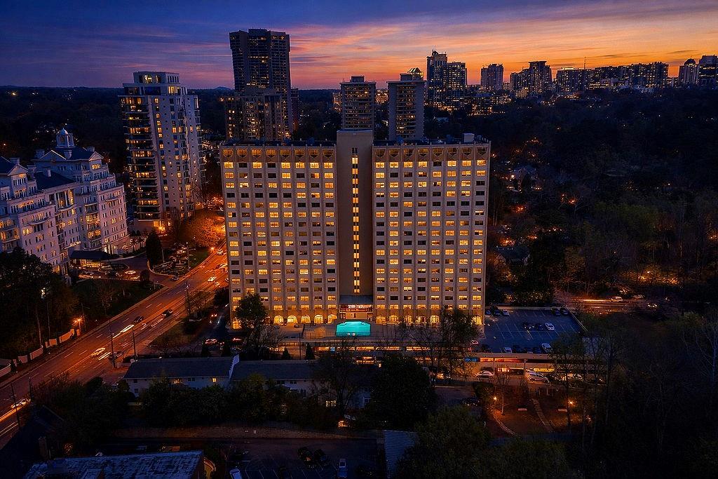 Atlanta skyline at dusk, with illuminated high-rises above tree-lined neighborhoods.