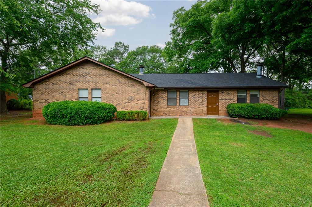 Single-story brick ranch home with a concrete walkway, trimmed shrubs, and mature trees.