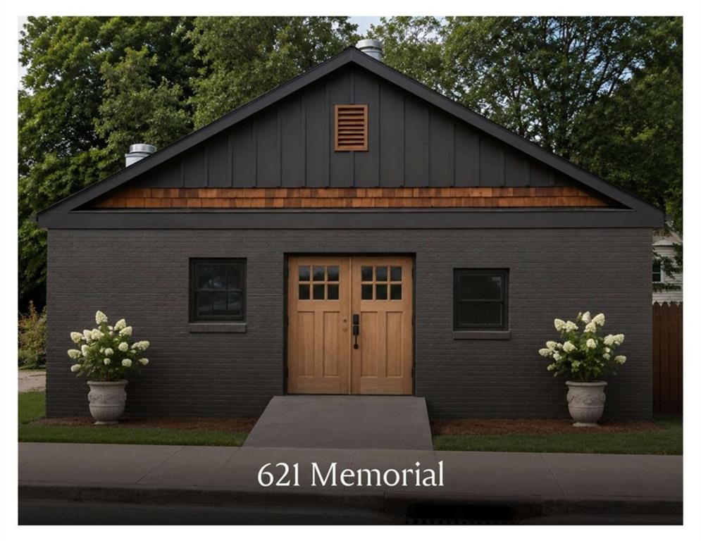 Dark brick home with a steep gabled roof, wooden double doors, and matching potted white flowers.