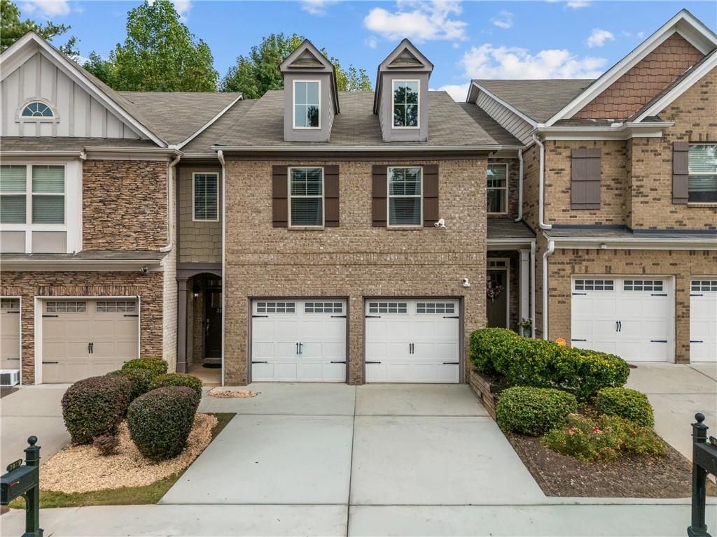 Brick townhouse with two garage doors, dormer windows, and landscaped front yard.