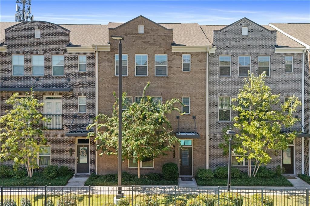 Brick townhomes with small balconies, young trees, and a black metal fence.