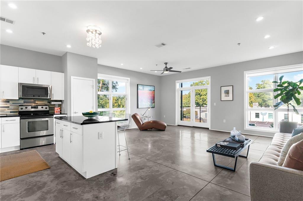 Open-plan kitchen and living room with white cabinetry, concrete floors, and large windows.